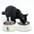 Black cat eating from a white Tiaki feeding bowl with two stainless steel dishes, one filled with wet food, the other empty.