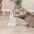 Katze interagiert mit einem weissen Spielzeugständer und rosa Drehmechanismus, geeignet für Beschäftigung oder Belohnungsspiele.