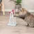 Kat bij interactief speeltuig van wit plastic met roze elementen en pinnen op de bodem, geschikt voor mentale stimulatie. Kat gebruikt poot om aan het speeltuig te bewegen.