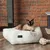 Cama para gatos Modern Living en blanco, con un gato siamés encima. Al fondo se ven un árbol rascador y un juguete de cuerda.