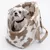 Sac de transport en tissu à motif tacheté beige et blanc, avec un petit chien blanc assis à l’intérieur, harnais noir visible, anse beige sur le côté.