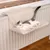 Cat bed made of soft fabric, attached to a radiator. White-grey cat lying relaxed on it.