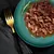 Chunks of meat in gravy served on a green plate with a sprig of rosemary, shown close up for product detail.