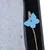 Détail d’un jouet en feutre bleu en forme de papillon attaché à une corde, fixé sur une surface en tissu gris et noir avec bouton métallique visible.