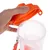 Transparenter Behälter mit orangefarbenem Deckel und Tragegurt, geöffnet und von einer Hand gehalten.