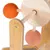 Détail d’un jouet pour chat en bois avec deux boules recouvertes de corde orange et rose fixées sur des tiges en bois, structure principale en bois clair et bambou.