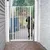 Barrière de sécurité blanche en métal installée entre deux murs, un grand chien à poil court se tient derrière la barrière sur une terrasse extérieure pavée.
