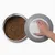 Hand opens grey lid of container with brown dry food pieces. Shows storage solution for pet food.