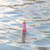 Schwimmendes Spielzeug in Form eines rot-weiss gestreiften Leuchtturms mit grüner Spitze auf Wasseroberfläche.
