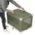 Caja de transporte verde con ventanas de malla y asas de transporte, levantada por una persona. Esquinas con tela reforzada.