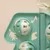 Détail d’un jouet interactif en plastique vert et blanc avec deux balles ajourées, motifs découpés visibles : note de musique, patte, étoile, tête de chat.