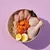 Bowl containing raw chicken breast, chicken drumstick, sliced carrots, brown rice, hard-boiled egg halves and a dark vegetable, showing visible ingredients of the product.
