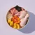 Bowl containing raw chicken drumstick, sliced carrots, potato pieces, rice, and a piece of seaweed, showing visible ingredients for pet food.