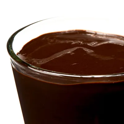 Staklena posuda napunjena tamnom, kremastom pastom ili umakom. Nema vidljivih oznaka brenda ni teksta.