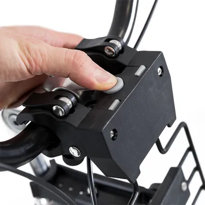 Primo piano di una mano che preme un pulsante grigio su un supporto nero fissato al manubrio di una bicicletta, con leve e viti visibili.