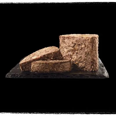 Blok natvoer in plakken gesneden, zichtbaar grove structuur, gepresenteerd op een zwarte leisteen. Geen merknaam of verpakking zichtbaar.