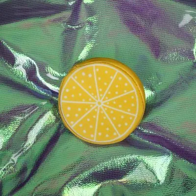 Ronde gele accessoire met citroenmotief, zichtbaar op glanzende ondergrond. Materiaal niet duidelijk herkenbaar.