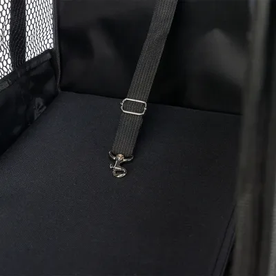 Intérieur d’un panier ou siège pour animal en tissu noir avec sangle réglable et mousqueton métallique, paroi latérale en maille visible à gauche.