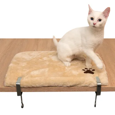 Beige kattenligbed met pluche bekleding en pootafdrukmotief, bevestigd aan een tafelrand. Witte kat zit erop.
