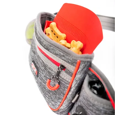 Marsupio KONG grigio con cerniera rossa, riempito con snack a forma di osso per cani. Tasca laterale per accessori visibile.