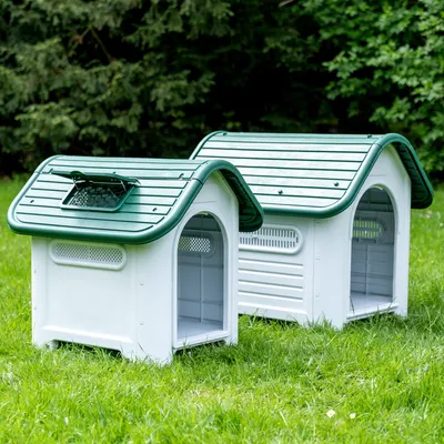 Due cucce per cani bianche in plastica con tetto verde, prese d’aria e coperchio rimovibile, posizionate su un prato.