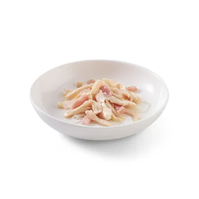 Vit skål med fina strimlor av kycklingkött och rosa bitar i gelé, serveringsklar.