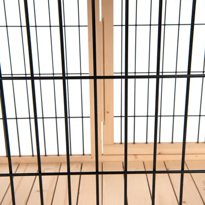 Vue rapprochée d’une structure en métal noir avec fond et cadre en bois clair, montrant les matériaux utilisés pour une cage ou un enclos.