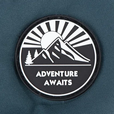 Badge with mountain, sun and trees illustration, featuring the text 'ADVENTURE AWAITS'.