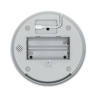 Rückseite eines runden Geräts mit Batteriefach für zwei AA-Batterien, Lautsprecheröffnung und USB-Anschluss. Sichtbare Federn und Plus-Minus-Markierungen im Fach.