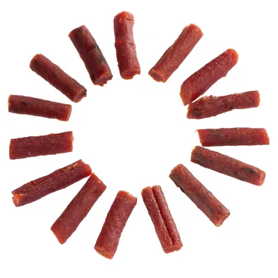 Bâtonnets rouges de friandises pour animaux, disposés en cercle sur fond blanc. Aucun emballage ou marque visible.