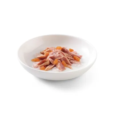 Ciotola bianca con bocconcini di carne rosa e pezzetti arancioni in gelatina, alimento umido per pet visibile senza confezione.
