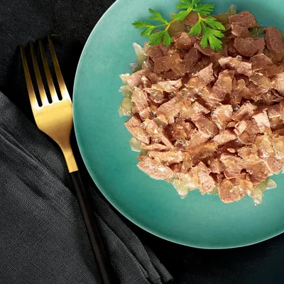 Chunks of wet pet food in jelly served on a green plate, garnished with fresh herbs.