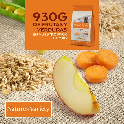 Nature’s Variety Original. 930G DE FRUTAS Y VERDURAS EN NUESTRO PACK DE 2 KG. На изображении яблоко, морковь, зёрна и упаковка корма. Текст на испанском языке.