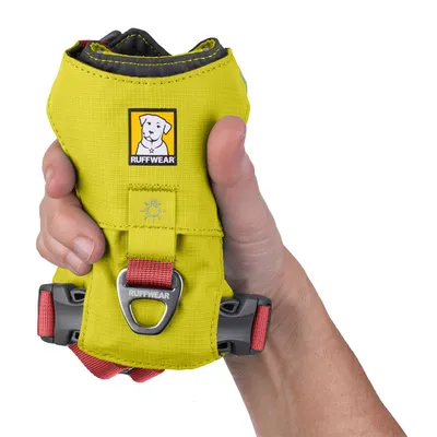 Ruffwear Hundegeschirr in Gelb mit rotem Verschluss und Metallring, gehalten in einer Hand. Logo mit Hund sichtbar.