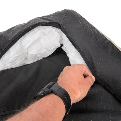 Main ouvrant une housse noire à fermeture éclair, révélant un intérieur en tissu blanc rembourré. Matières visibles : tissu synthétique noir et blanc.