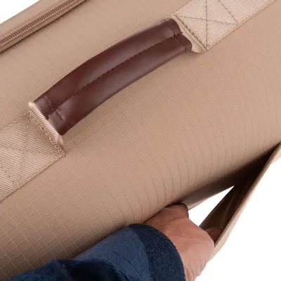 Detailný záber na hnedé kožené držadlo a ruku otvárajúcu bočné vrecko z béžovej látky.