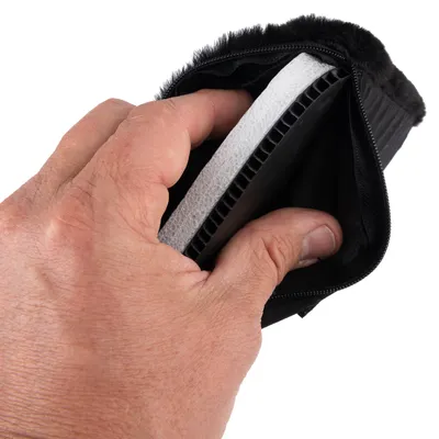 Hand houdt een zwart product met ritssluiting, dat een witte en zwarte laag van kunststof en schuim toont.