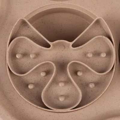 Close-up of a beige anti-gulping bowl with multiple indentations and elevations for slow food intake.