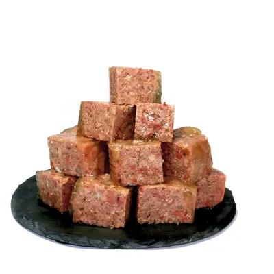 Ułożone w stos kostki z wilgotnego mięsa, podane na czarnym talerzu. Pokazuje strukturę i konsystencję produktu.