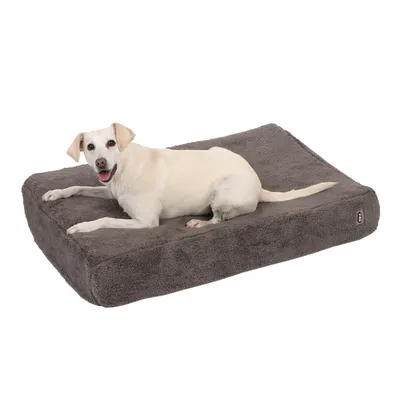 Hund liegt auf einem grauen, flauschigen Hundebett mit rechteckiger Form. Kleine Markenetikette sichtbar an der Seite des Bettes.