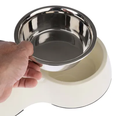Hand lifts a removable stainless steel bowl from a white feeding dish with non-slip base.