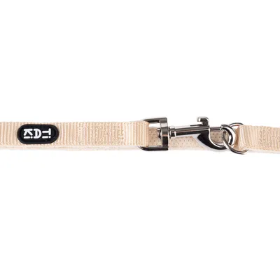Beige Hundeleine mit Metallkarabiner und schwarzem Logoaufnäher.