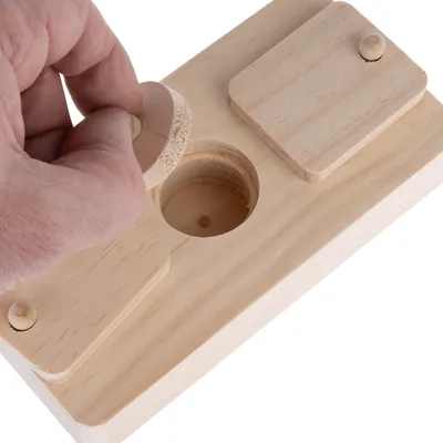 Juguete de madera con elementos móviles, una mano levanta una tapa redonda de madera de una cavidad. Adecuado para juego o entrenamiento interactivo.