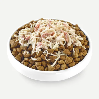 Bowl with brown dry food pieces, topped with shredded white and pink meat.