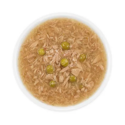 Lähikuva märkäruoasta, jossa on pilkottua lihaa ja vihreitä herneitä valkoisessa kulhossa.