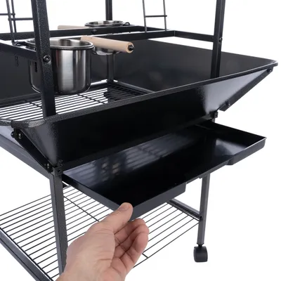 Schwarzer Metallkäfig mit herausziehbarer Schublade, zwei Edelstahl-Näpfen und Holzgriffen. Hand zeigt Funktion der Schublade.