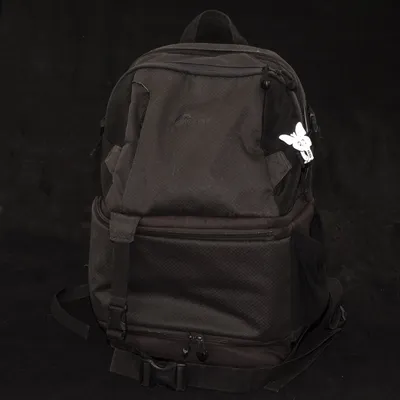 Mochila negra con varios bolsillos y un llavero de cabeza de perro blanca en la parte delantera.