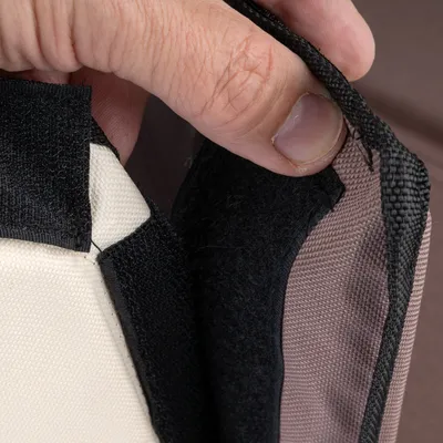 Close-up of a hook-and-loop fastener on brown fabric, open and held by a hand.