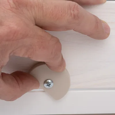 Main ajustant une molette en plastique beige fixée par une vis sur une surface en bois clair. Aucun texte ou marque visible.