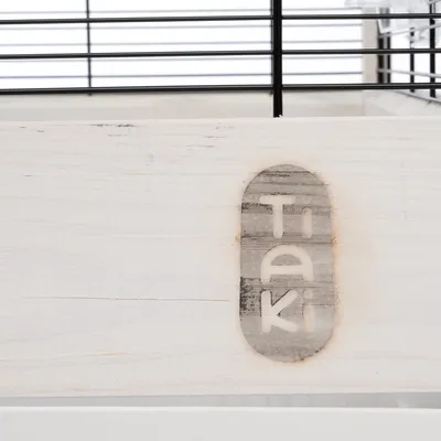Inscription visible : Tiaki sur une surface en bois clair, barreaux métalliques noirs en arrière-plan.